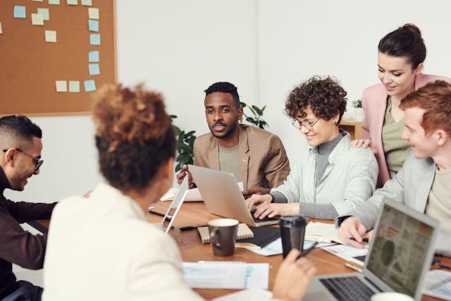 Group of people sitting around a table with laptops and documents